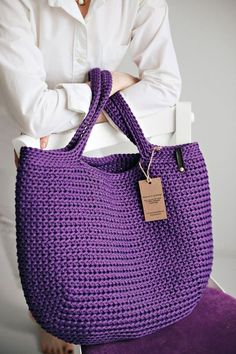 a woman holding a purple crocheted bag with a tag on it's handle