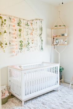 a white crib with flowers hanging on the wall and a baby's bed next to it