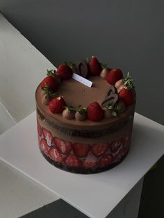 a chocolate cake topped with strawberries on top of a white countertop next to a window