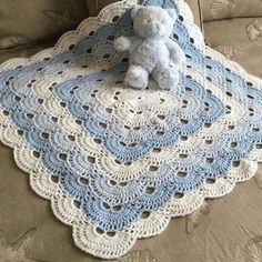 a teddy bear sitting on top of a crocheted blue and white afghan blanket