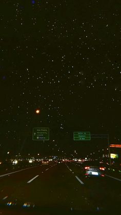 the night sky is filled with stars and street signs as cars drive down the road
