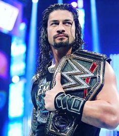 a man with long hair wearing a wrestling belt and giving the thumbs up sign in front of him