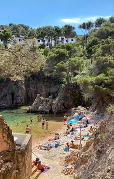 people are on the beach and in the water near some rocks, trees and buildings