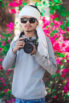 a young man taking a photo with his camera in front of colorful flowered trees