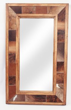 a wooden mirror sitting on top of a white wall next to a brown cowhide rug