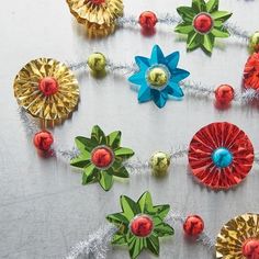 colorful paper flowers and bells are arranged on a white tablecloth with tinsel wrapped around them