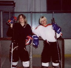 two people standing next to each other holding hockey equipment