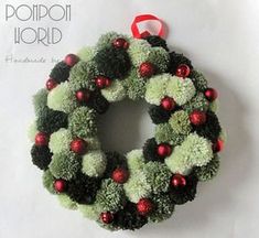 a green and red christmas wreath hanging on the wall next to a white sign that says pompom world