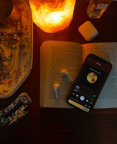 an open book and earbuds on a table next to a lit candle, cell phone and glass