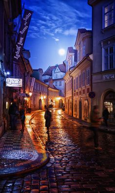 people are walking down the cobblestone street at night in an old european town