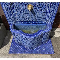 a blue tiled fountain with water coming out of it's sides and a gold faucet in the center