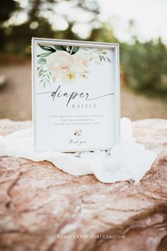 a sign that is sitting on top of a rock with white flowers and greenery