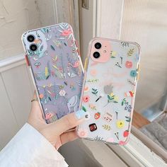 two cases with flowers on them are held up in front of a window by someone's hand