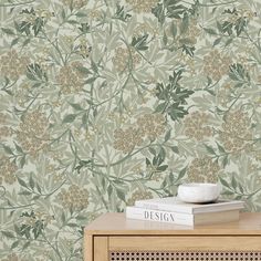 a table with books on top of it next to a wallpapered background that has flowers and leaves