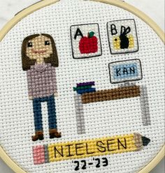 a cross stitch pattern with a girl holding a pencil in front of a school desk