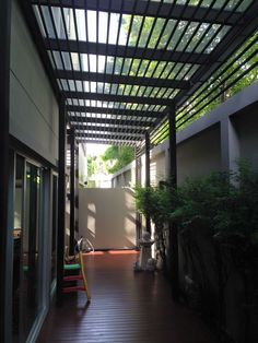 an outdoor covered patio with wooden flooring and plants on either side of the pergolated area