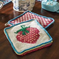 two crocheted strawberry coasters sitting on top of a table next to a cup