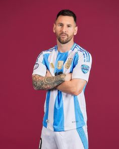 a man with tattoos standing in front of a red background wearing a blue and white shirt