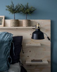 a bedroom with blue walls and wooden shelves on the wall, two planters above the bed