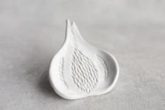 a white porcelain object with wavy lines on it's side, sitting on a gray surface