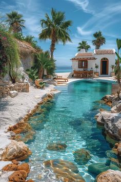 an outdoor swimming pool surrounded by rocks and palm trees with a house in the background