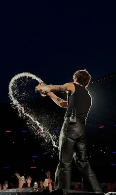 a man standing on top of a stage holding an object in his hand and spraying it with water