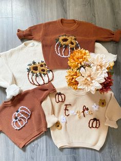 three sweaters with flowers and pumpkins on them are laid out on the floor