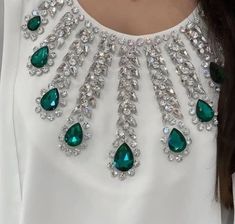 a woman wearing a white top with green jewels on it