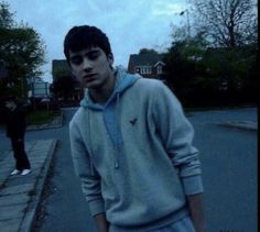 a young man standing on the side of a road next to a person wearing a hoodie