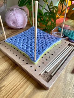 knitting needles and yarn on a wooden board with crochet squares in the background