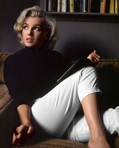 a woman sitting on top of a couch next to a book shelf