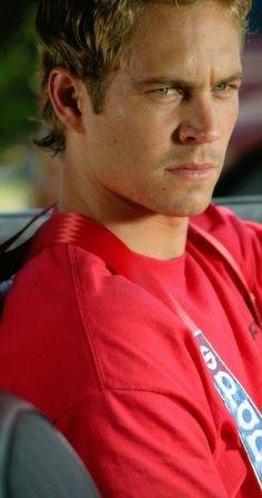 a young man in a red shirt is sitting in a car and looking off to the side