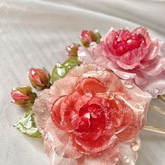 three pink and red flowers sitting on top of a white cloth covered tablecloth with water droplets