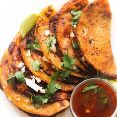 some tacos are on a white plate with sauce and cilantro garnish