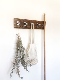 two white bags hanging on a wall next to a wooden coat rack with metal hooks