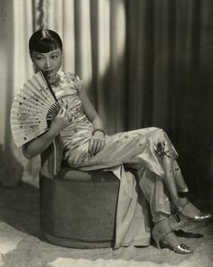 an old photo of a woman sitting on a stool with a fan in her hand