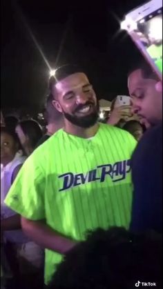 a man with a beard wearing a neon green baseball jersey standing in front of a crowd