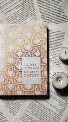 two candles sitting on top of an open book next to some folded up pages with the title f scott fitzgerald's the great gatsby