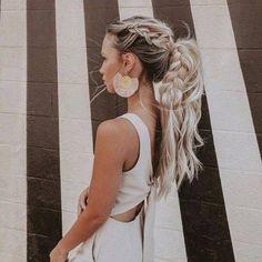 a woman standing in front of a wall with her hair in a pony tail braid