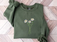 a green sweatshirt with daisies embroidered on the front and back, sitting on a wood floor