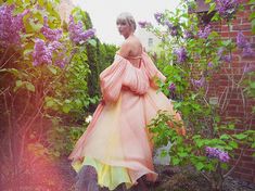 a woman in an off - the - shoulder dress is walking through some bushes and flowers