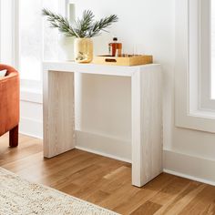 a white table with a plant on it in front of a window next to an orange chair