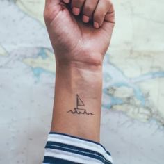 a person's arm with a small sailboat tattoo on the left side of their wrist