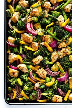 a pan filled with chicken, broccoli and red onion on top of a white table