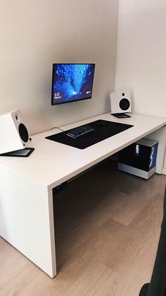 a desk with a computer monitor and speakers on it in front of a white wall