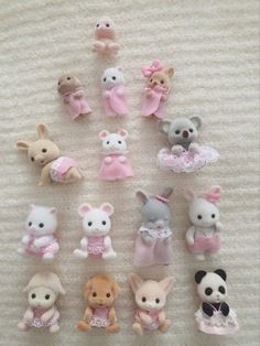 a bunch of small stuffed animals on a white blanket with pink and grey ones in them