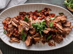 a white plate topped with sliced meat and garnished with cilantro sauce