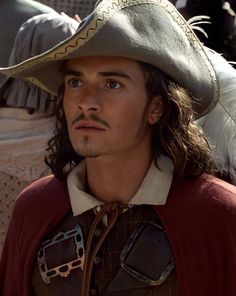 a man with long hair wearing a pirate hat and red shirt is looking at the camera