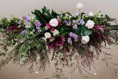 an arrangement of flowers and greenery hanging from the ceiling