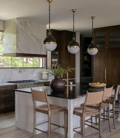 a kitchen with marble counter tops and dark wood cabinets, hanging lights above the island